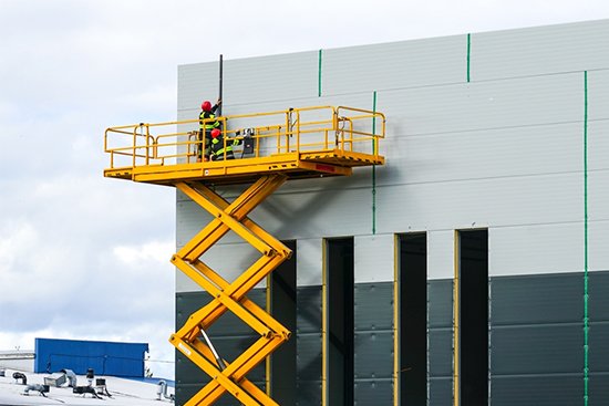 A man is working on a hydraulic scissor lift on a building.